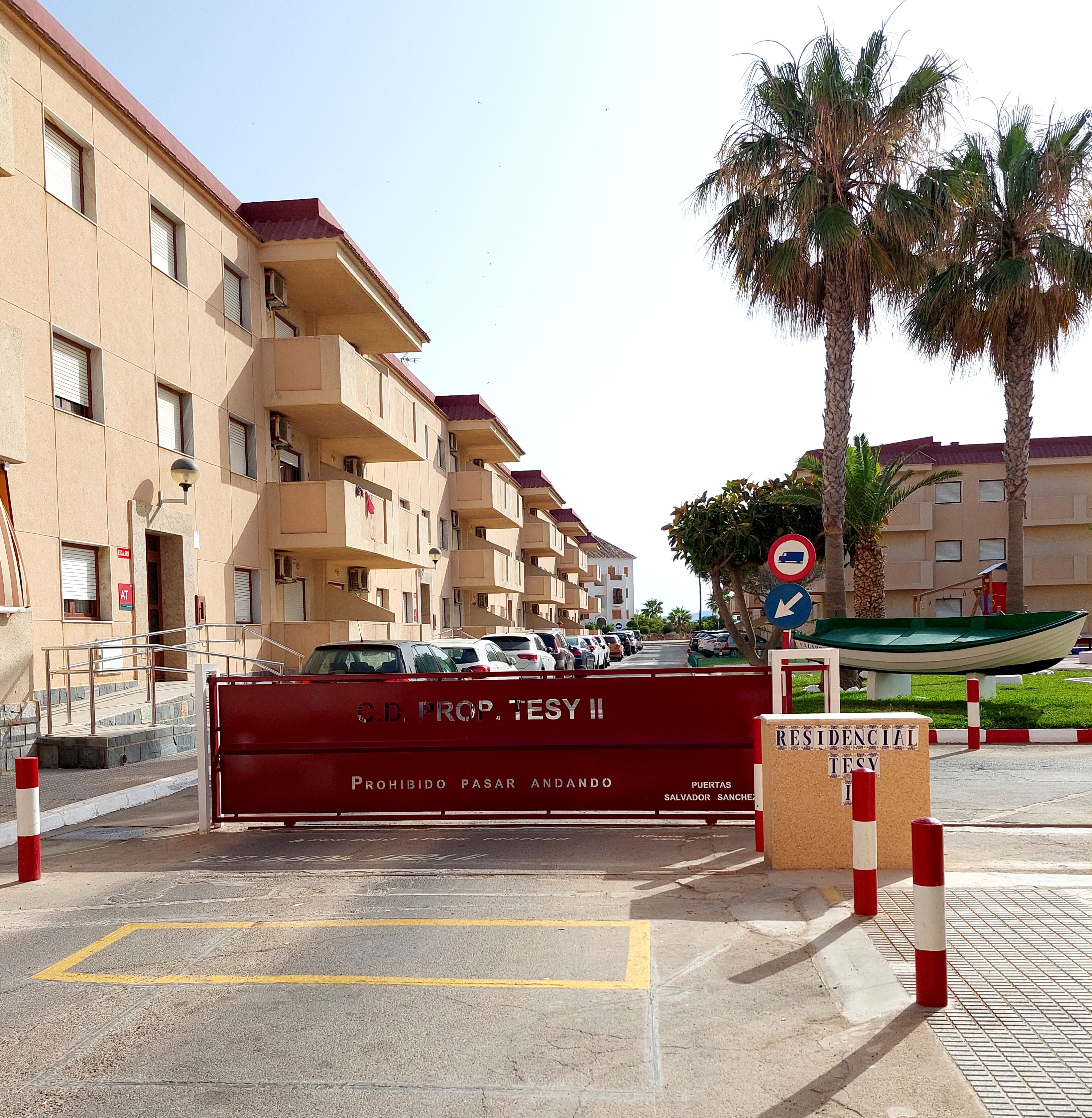 Zona residencial cerrada con una barrera roja, varios coches aparcados y un cartel de no estacionamiento.