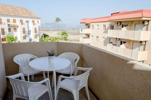 A balcony with a round table and four chairs, overlooking a beach and buildings with red roofs.