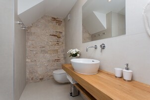 Ein Badezimmer mit Steinwand, Waschtisch aus Holz, weißem Waschbecken und Toilette.