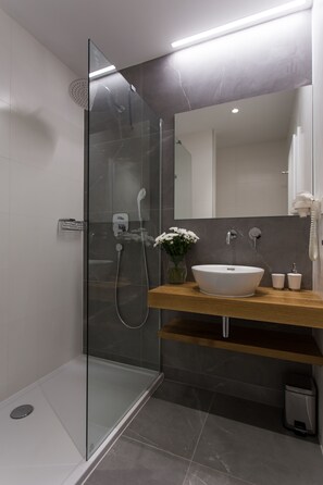 Un baño moderno con ducha envuelta en vidrio, un mueble de tocador de madera con lavabo blanco y un espejo grande.