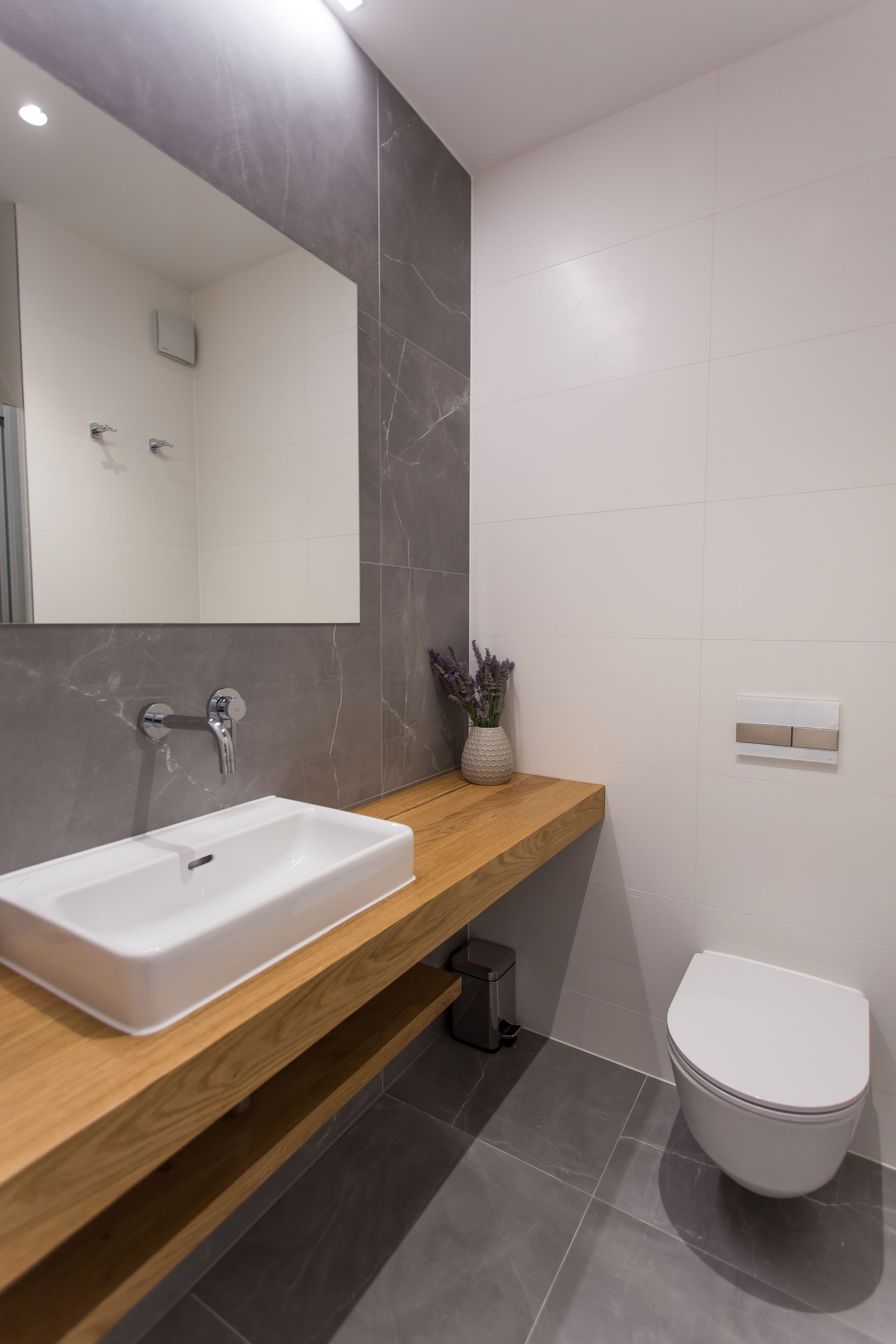 A modern bathroom with a white sink, wooden countertop, and a large mirror.