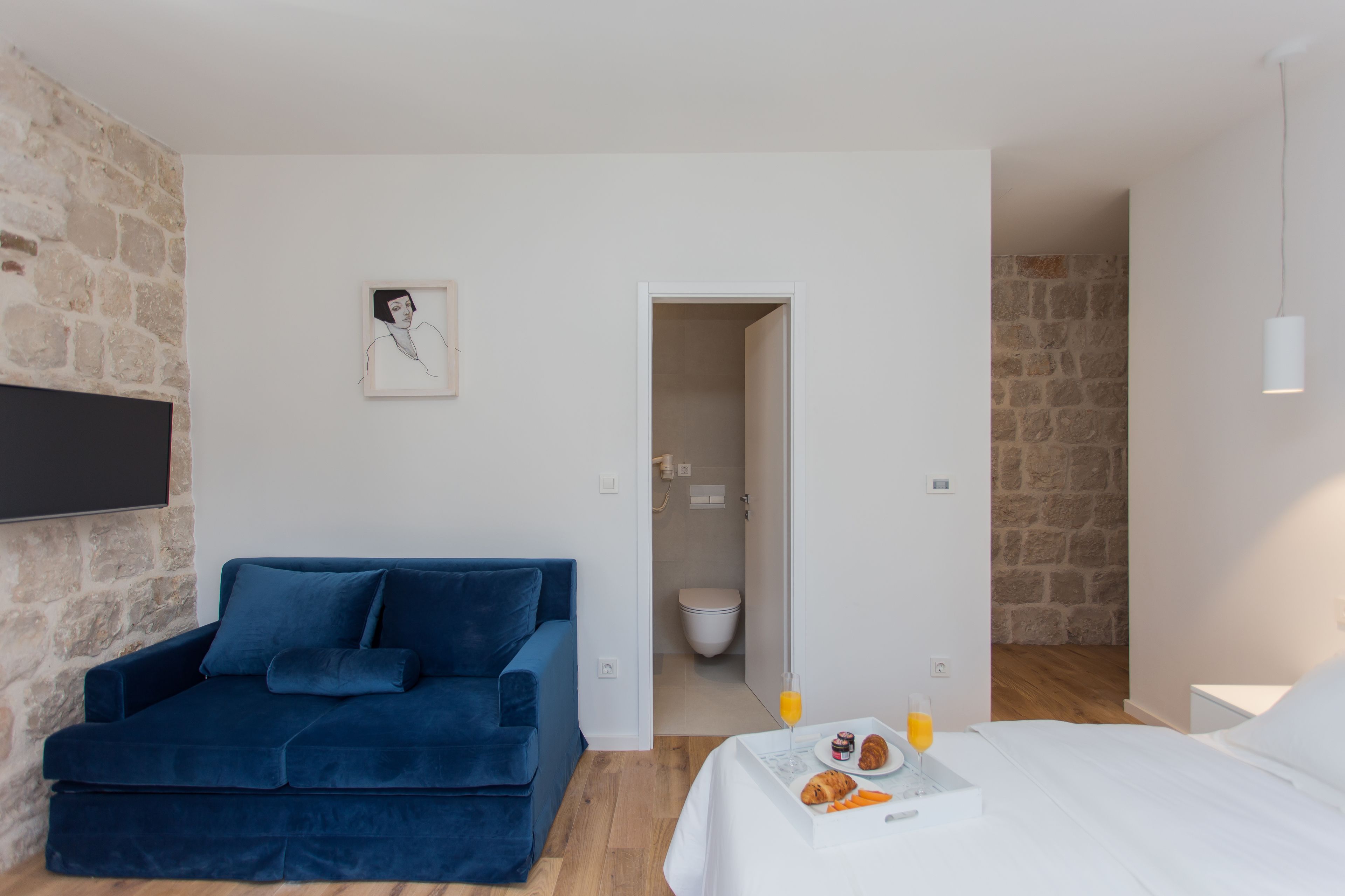 A modern room with a blue sofa, a bed, a breakfast tray, and a stone wall.