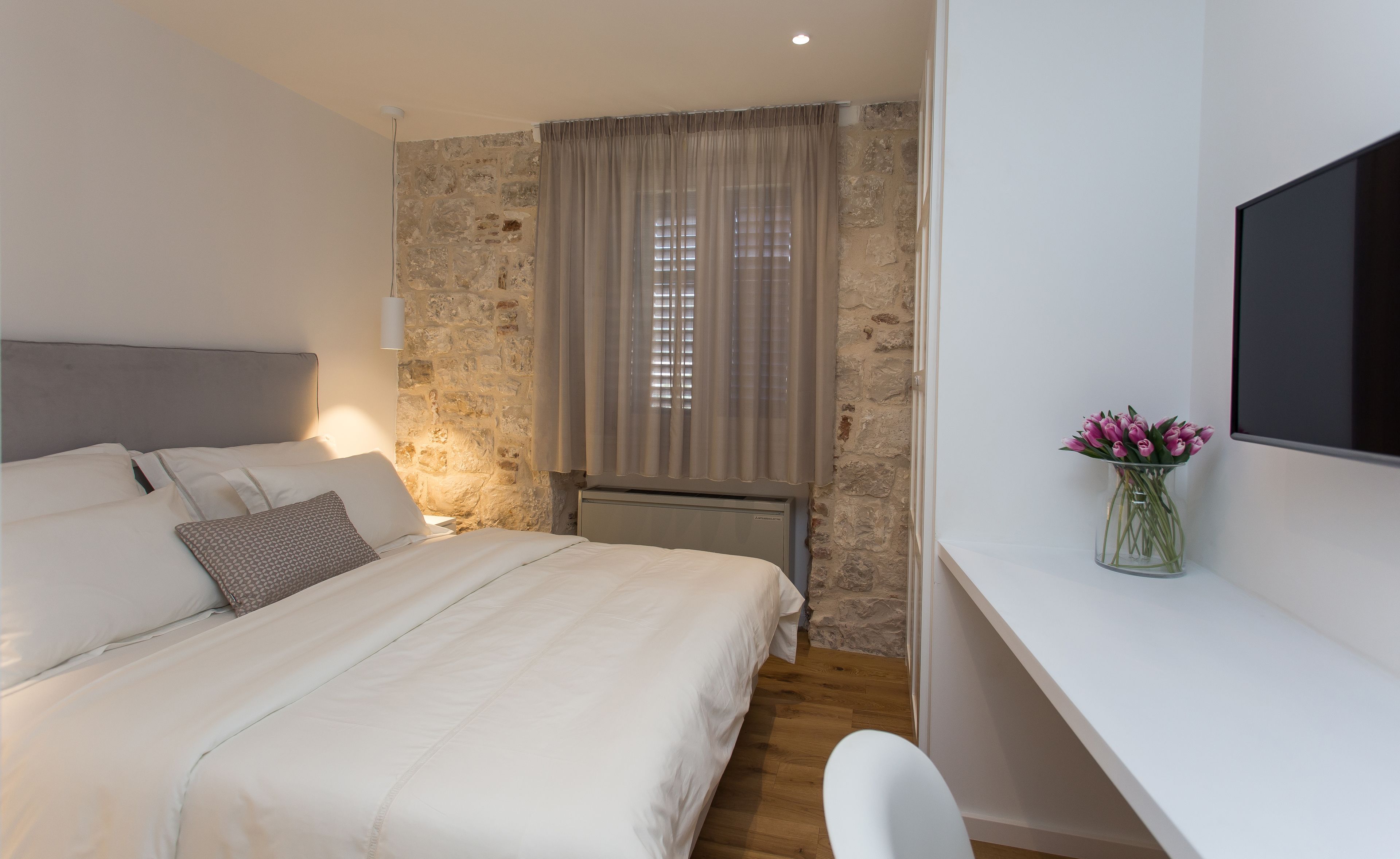 Un dormitorio con cama, escritorio, silla, televisor y ventana con cortinas.