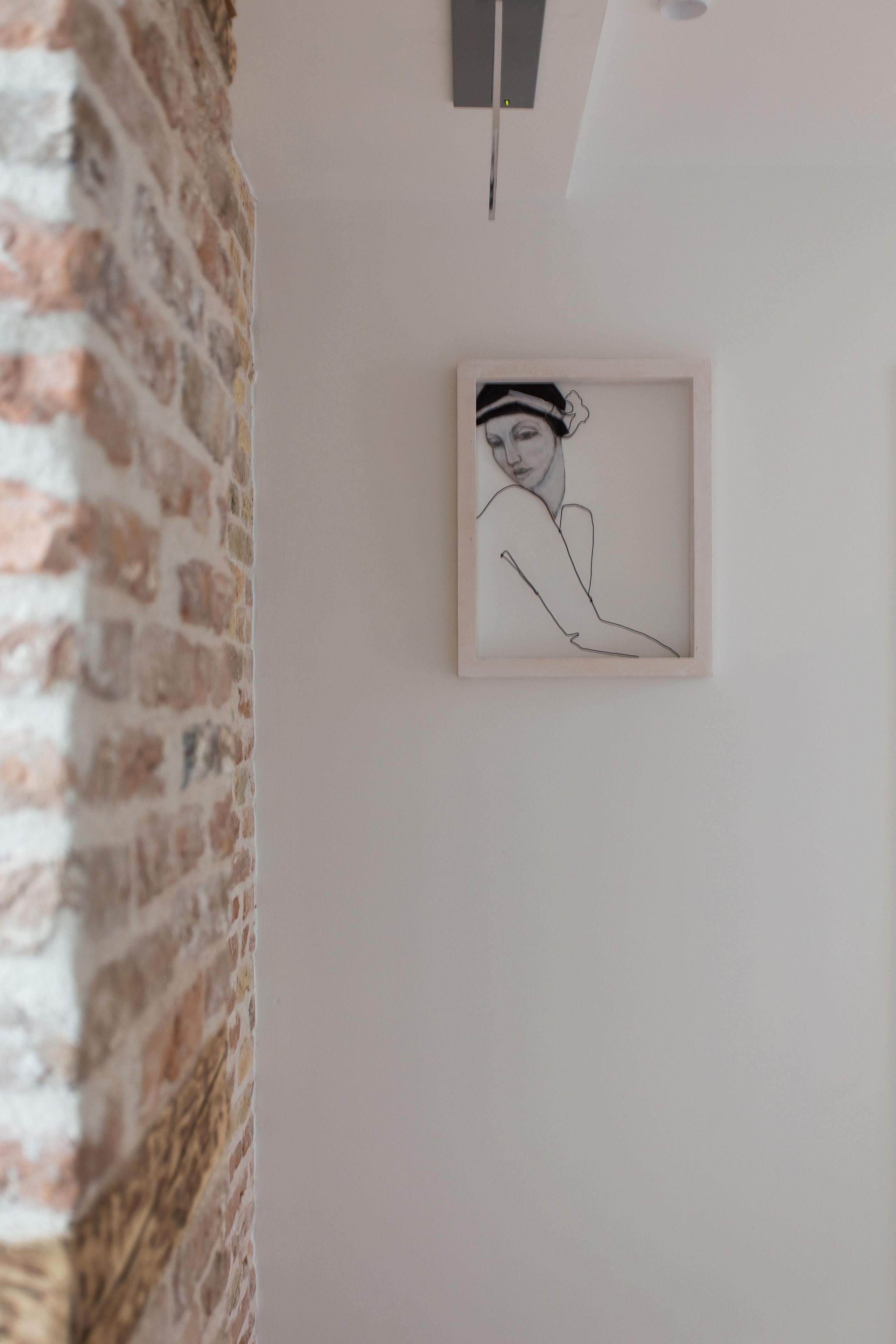 A framed line drawing on a white wall, a brick wall to the left, and a ceiling light fixture above.