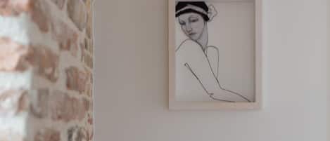 A framed line drawing on a white wall, a brick wall to the left, and a ceiling light fixture above.