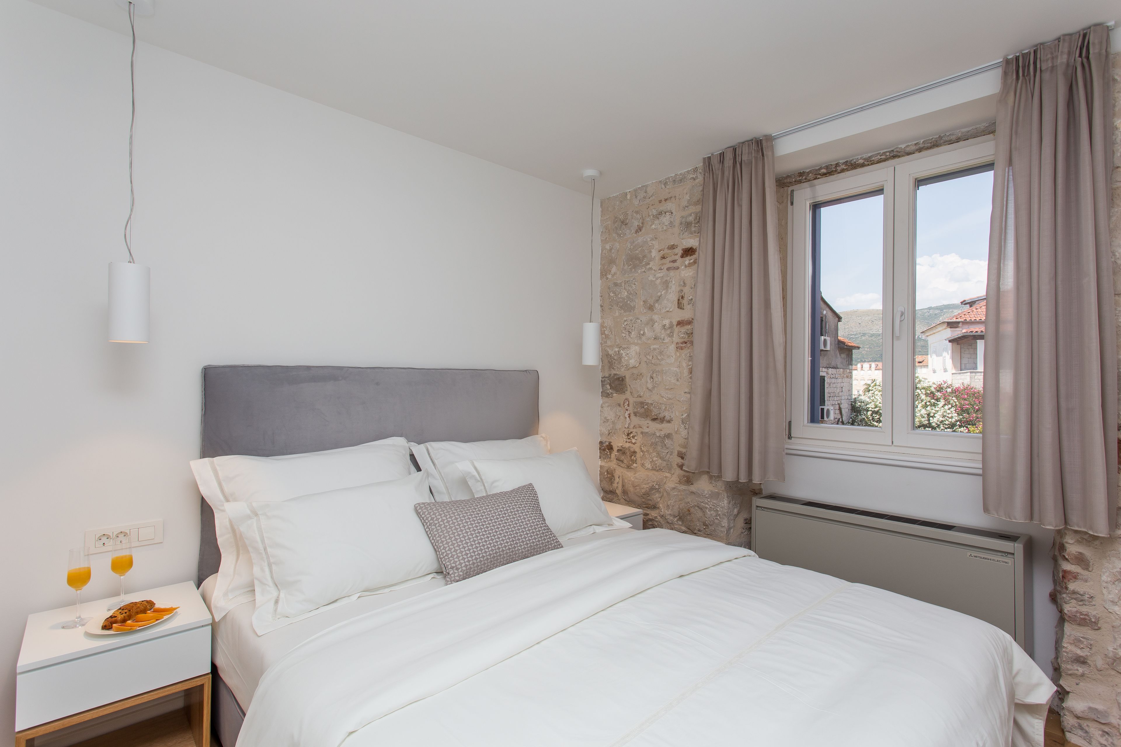A bedroom with a bed, a nightstand, a window with curtains, and a stone wall.