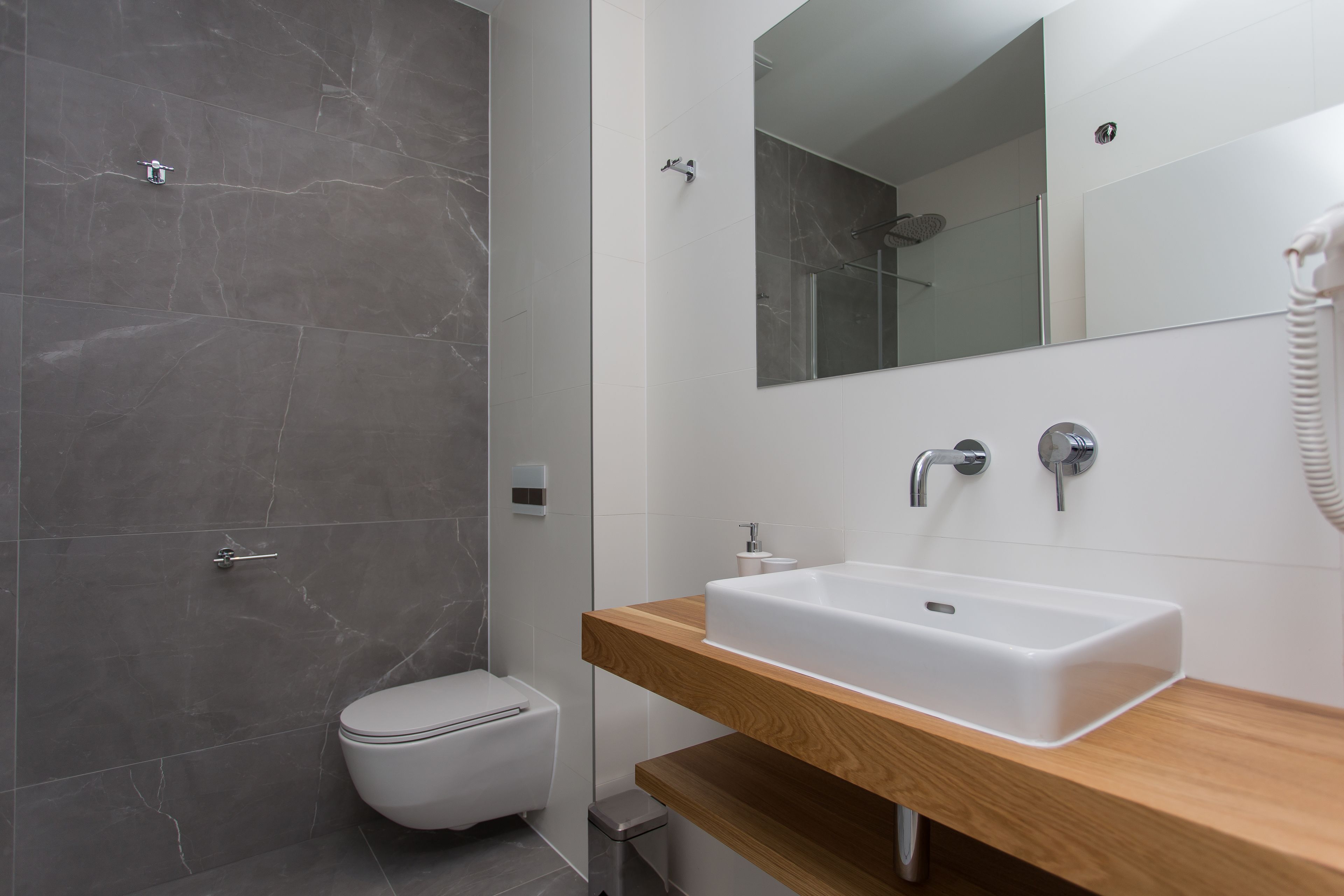 A modern bathroom with a marble shower, a white toilet, a wooden vanity with a sink, and a mirror.