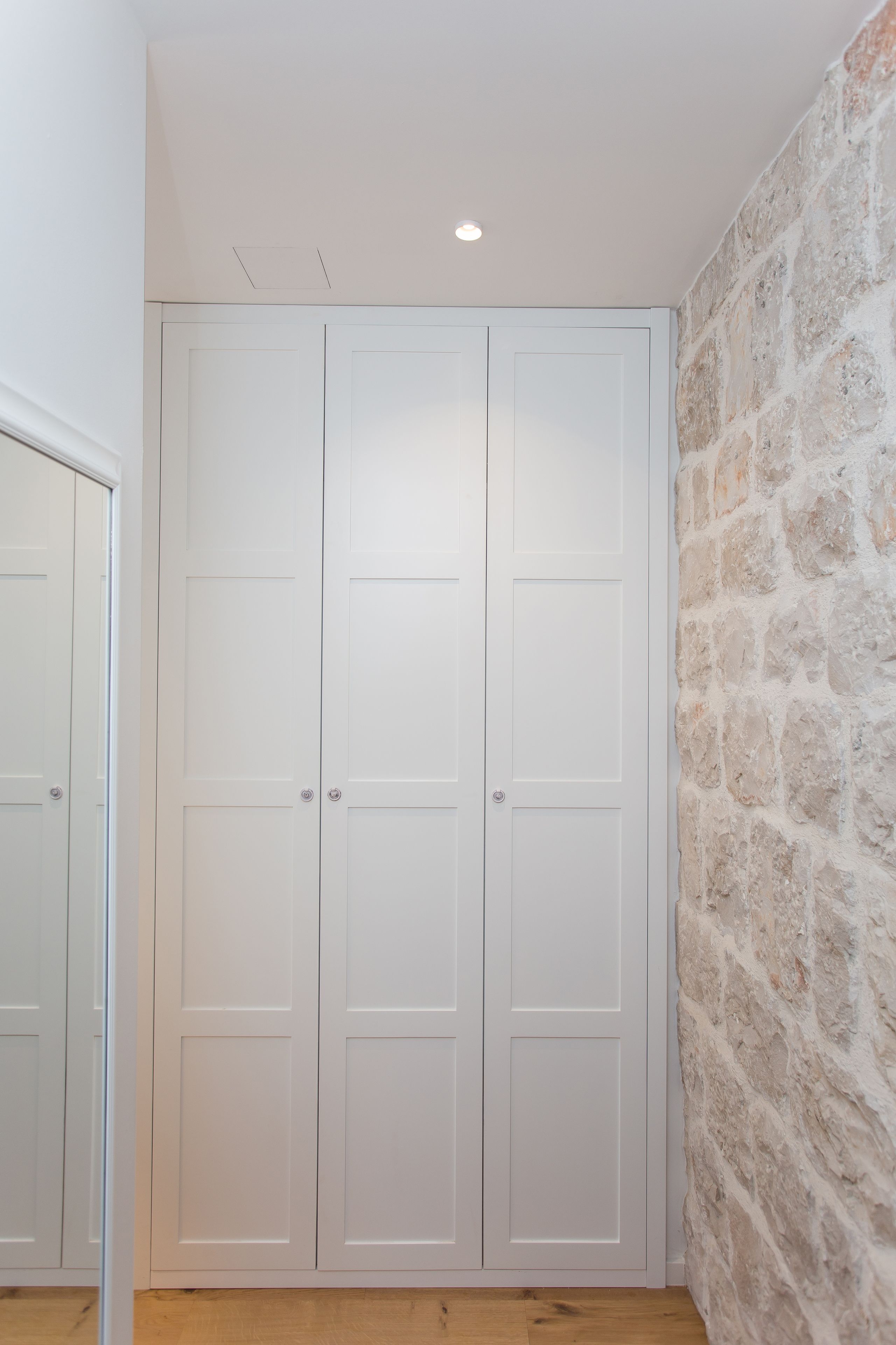 Un armario blanco con dos puertas y una pared de piedra.