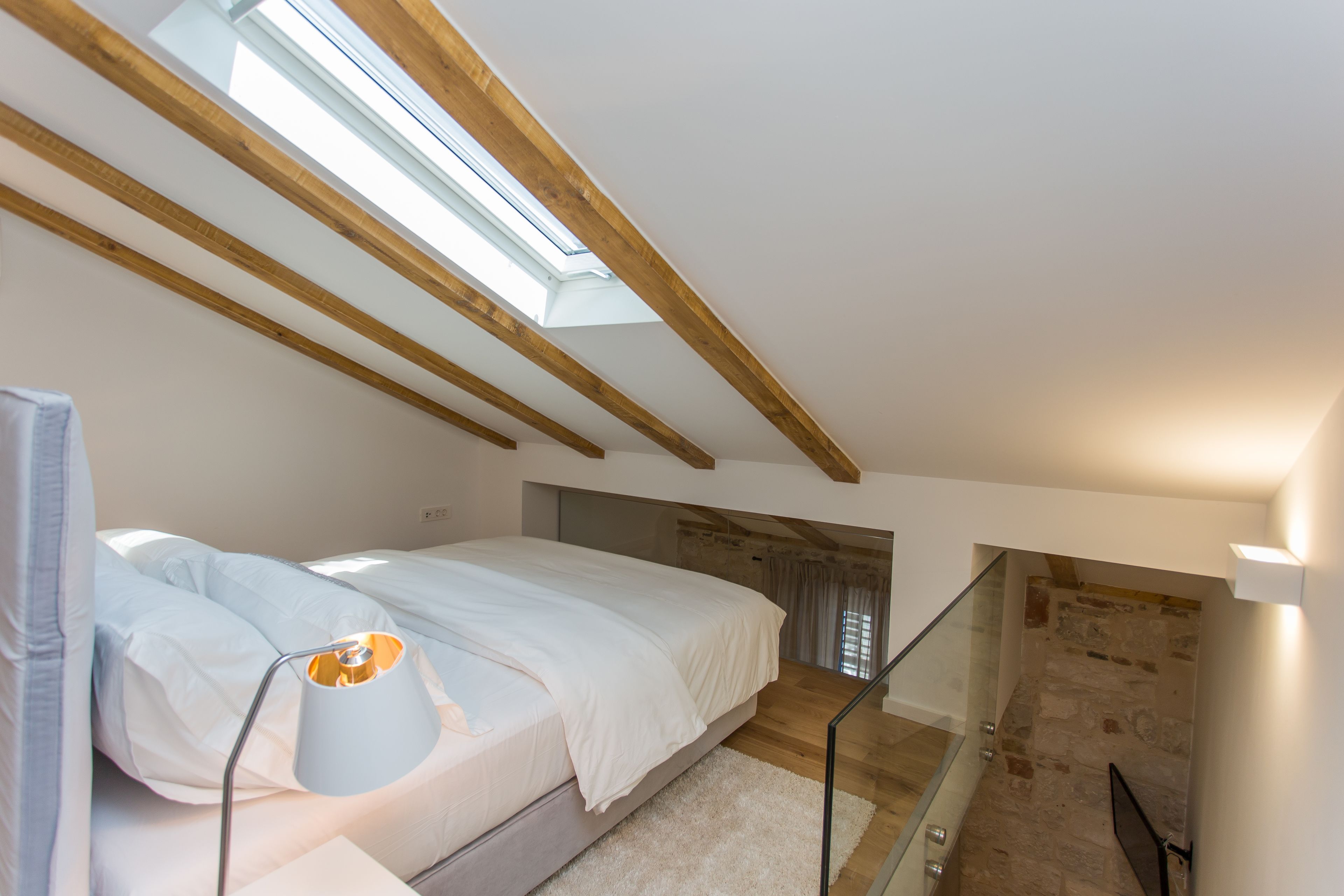 A bedroom with a skylight, a bed, a lamp, and a staircase.