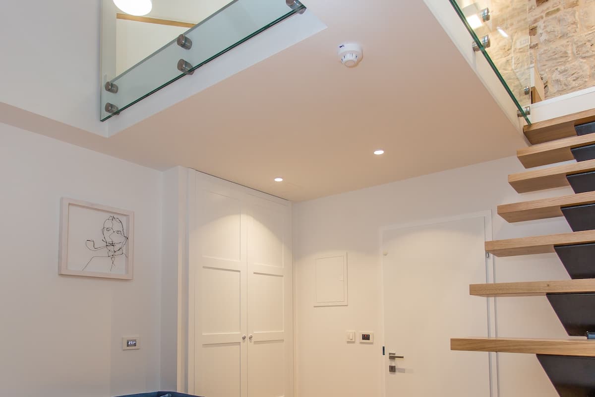 A modern living room with a blue sofa, a wooden coffee table with fruit, and a staircase with glass railings.
