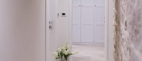 Un pasillo con paredes blancas, vigas de madera, una puerta blanca y un jarrón con flores.