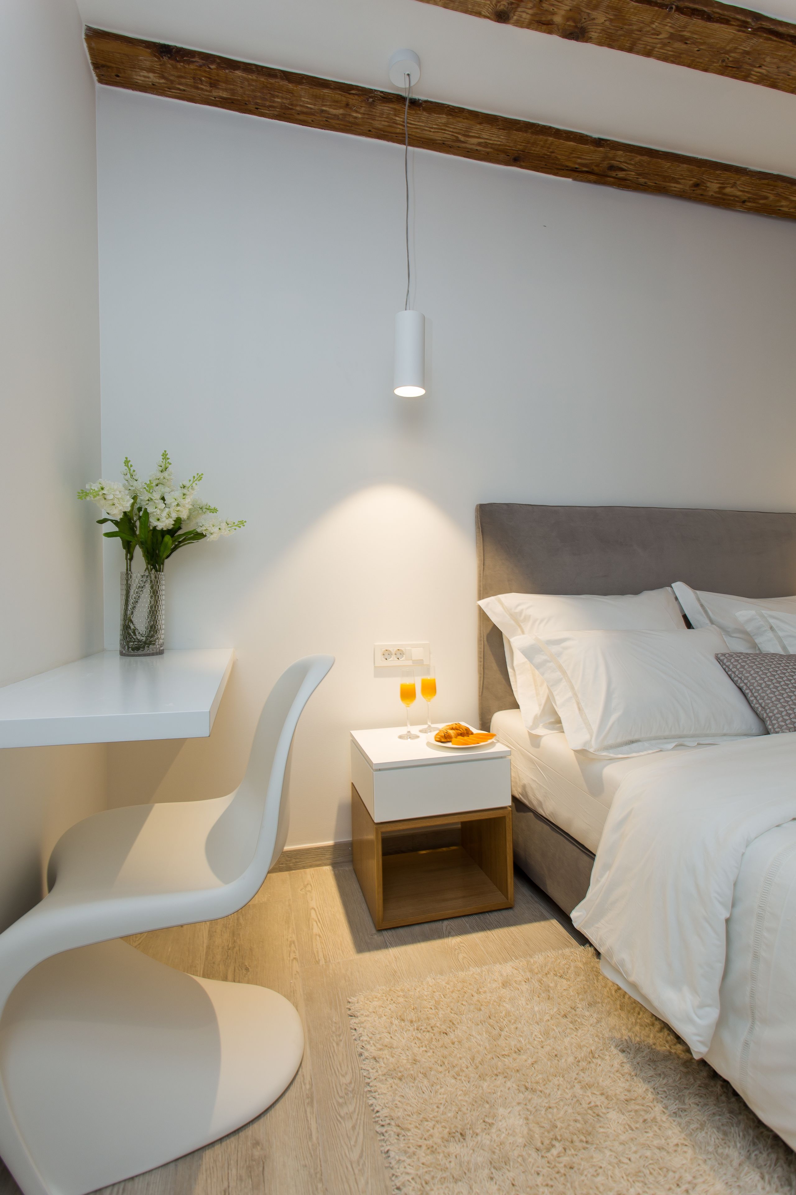 A modern bedroom with a bed, bedside table, and a white chair.