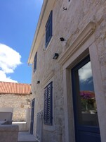 Ein Gebäude aus Stein mit Ziegeldach, Fensterläden und einem Fenster mit Blick auf violette Blumen.