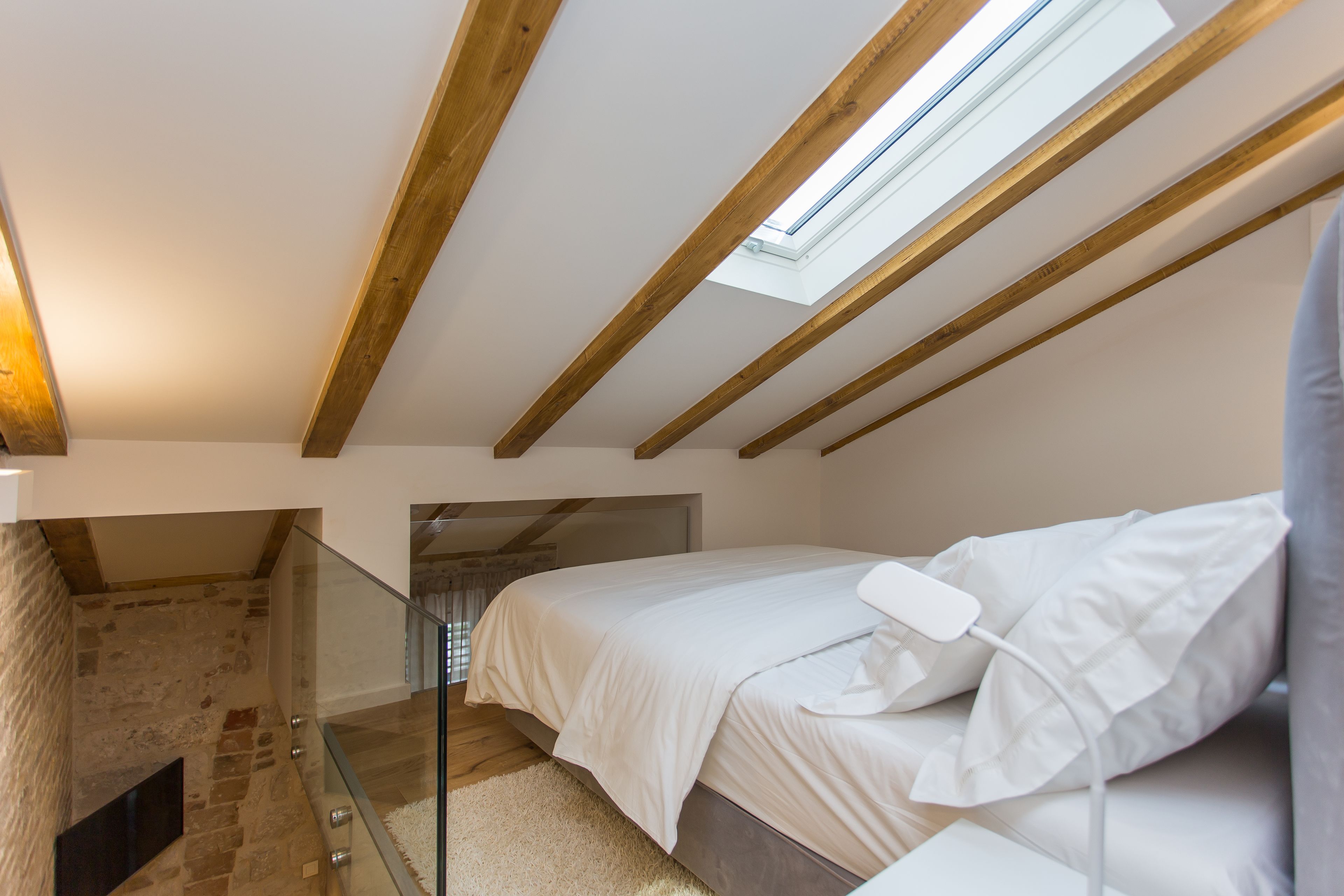 A bedroom with a sloped ceiling, a skylight, a bed, and a stone wall.