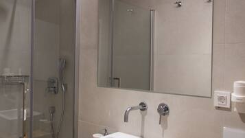 Un baño moderno con ducha envuelta en vidrio, un lavabo blanco y un mueble de tocador de madera.