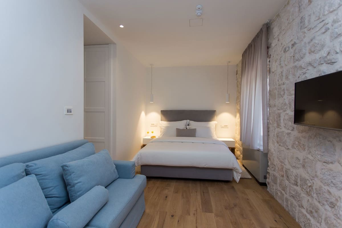A bedroom with a bed, bedside tables, a blue sofa, and a stone wall.