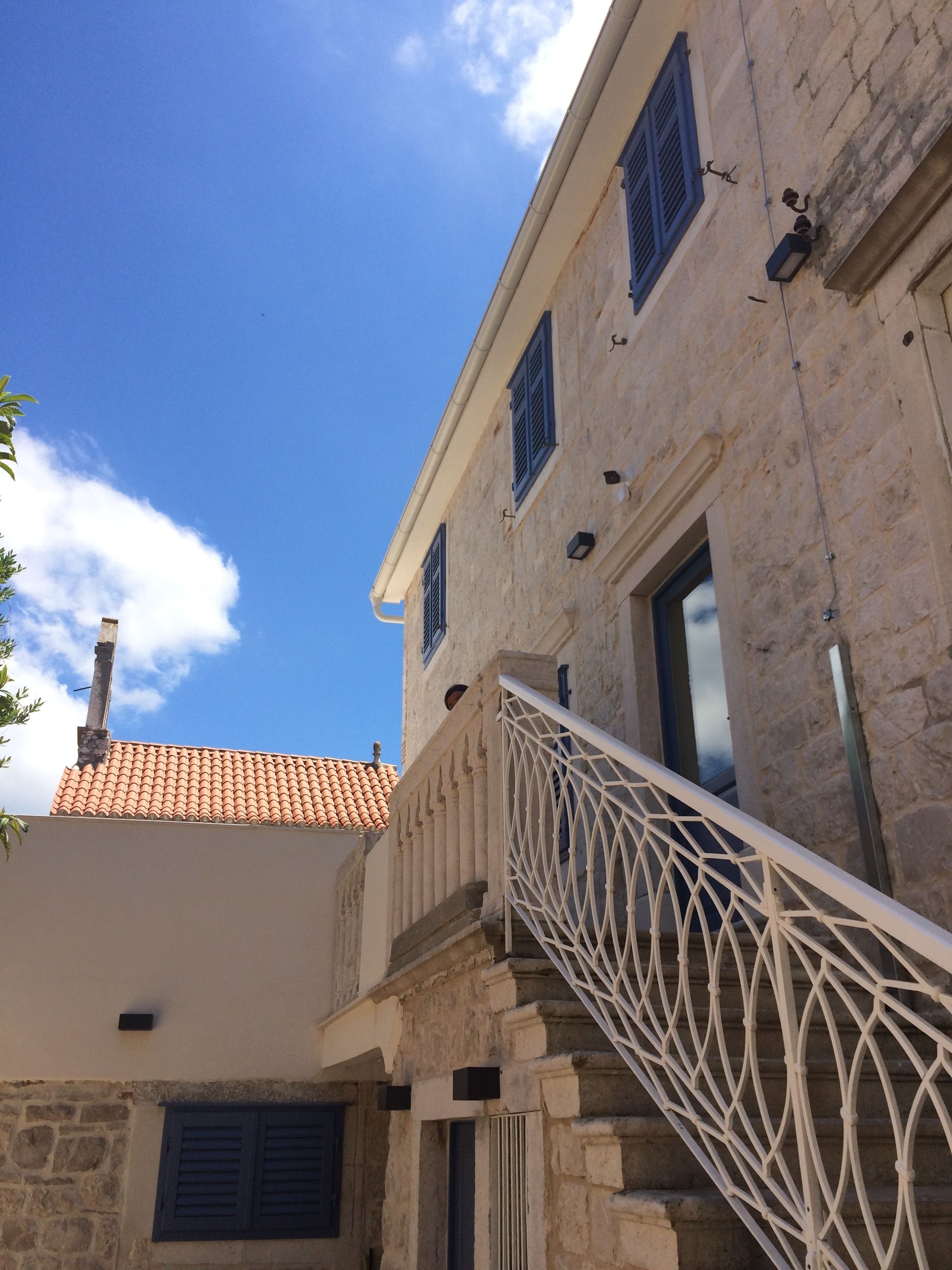 A stone building with a tiled roof, a white railing, and a clear blue sky.