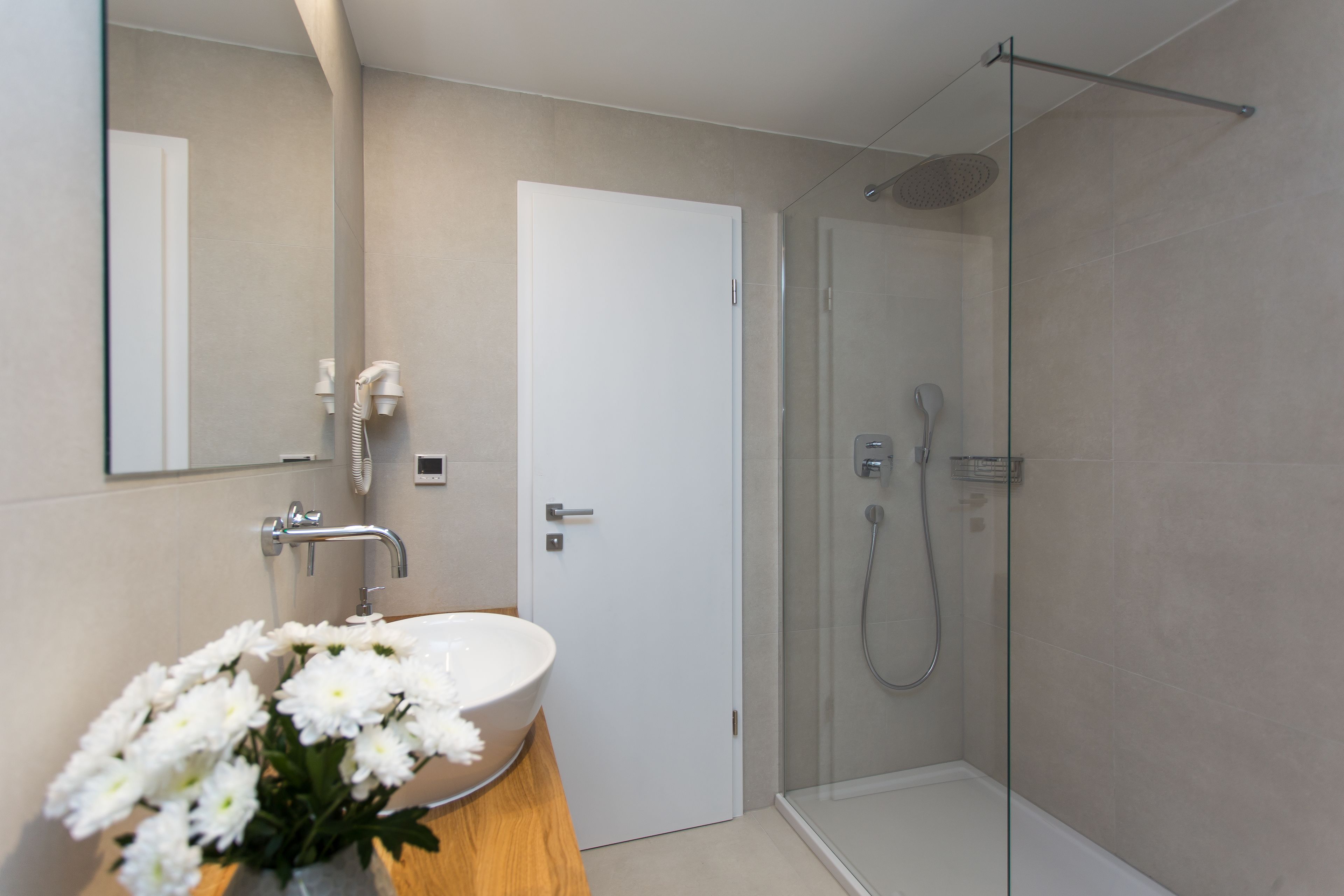 A modern bathroom with a white sink, a glass shower enclosure, and a door leading to another room.