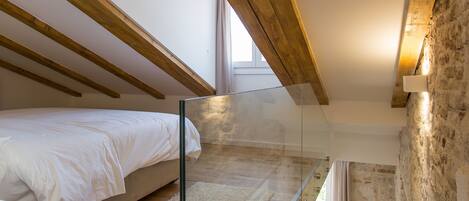 Un dormitorio con literas, vigas de madera, un separador de vidrio, un escritorio pequeño y una pared de piedra.
