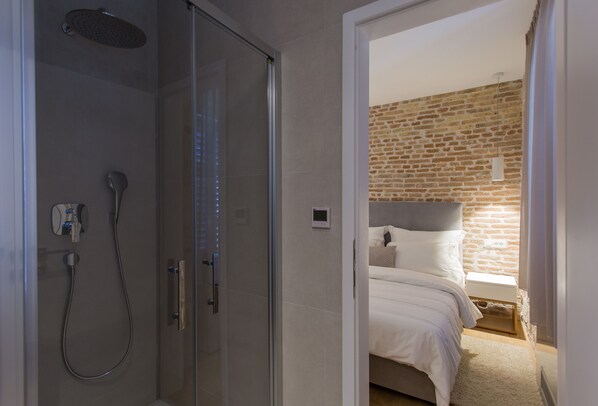 Un baño moderno con cabina de ducha de vidrio, un cabezal de ducha manual y un panel de control en la pared.