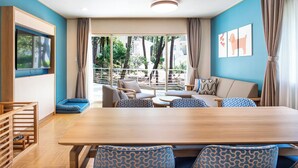 A modern room with a wooden dining table, blue patterned chairs, a sofa, and a view of a garden through large windows. - Seagaia Forest Cottages (Miyazaki)