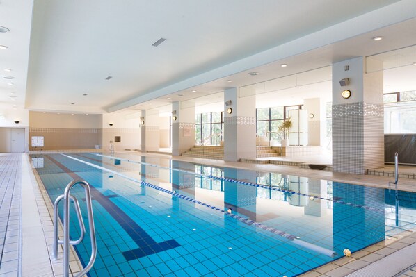 A large indoor swimming pool with clear lanes, a lifeguard chair, and a tiled floor. - Seagaia Forest Cottages (Miyazaki)