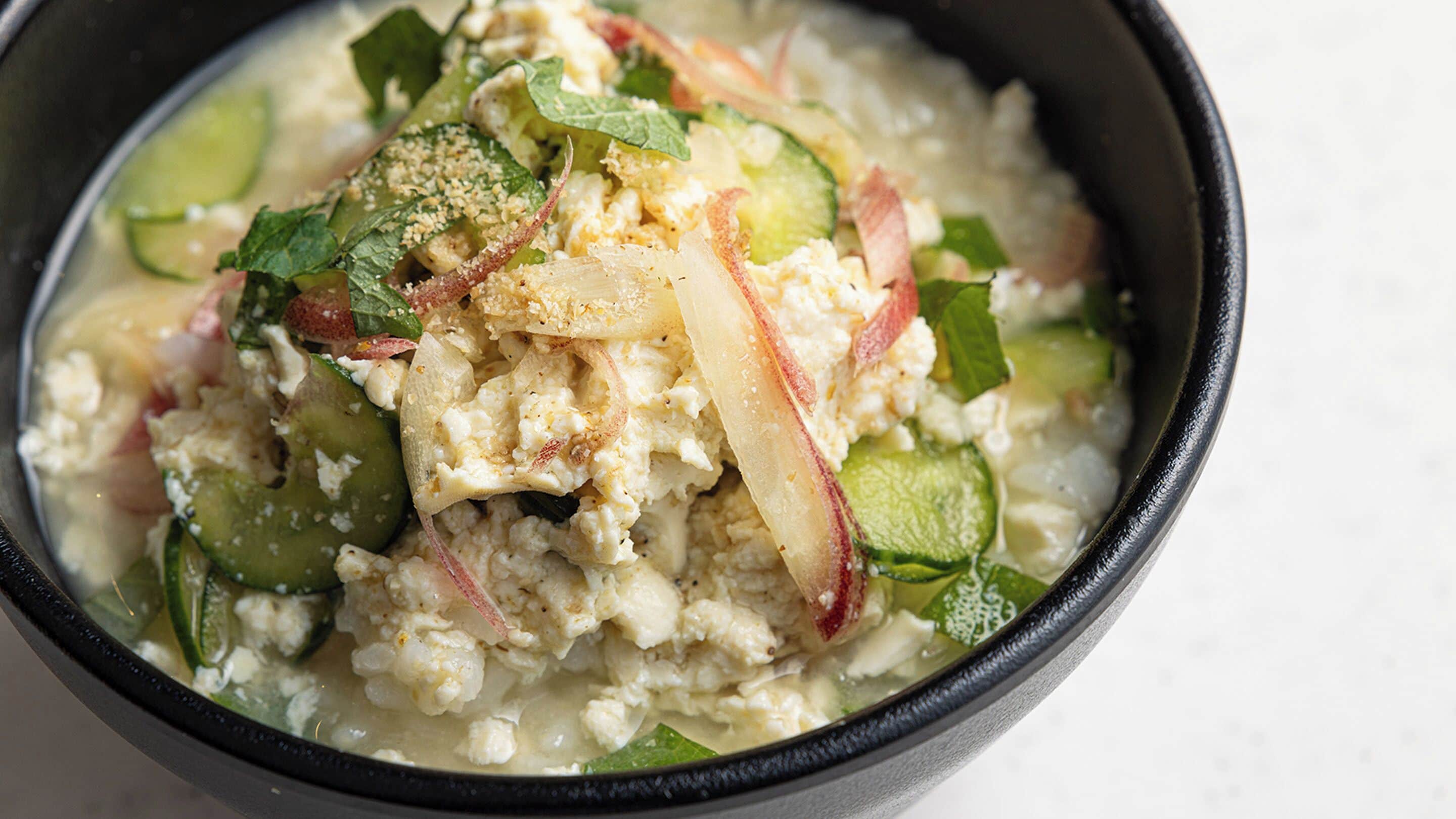 A bowl of food with various vegetables and a creamy sauce.