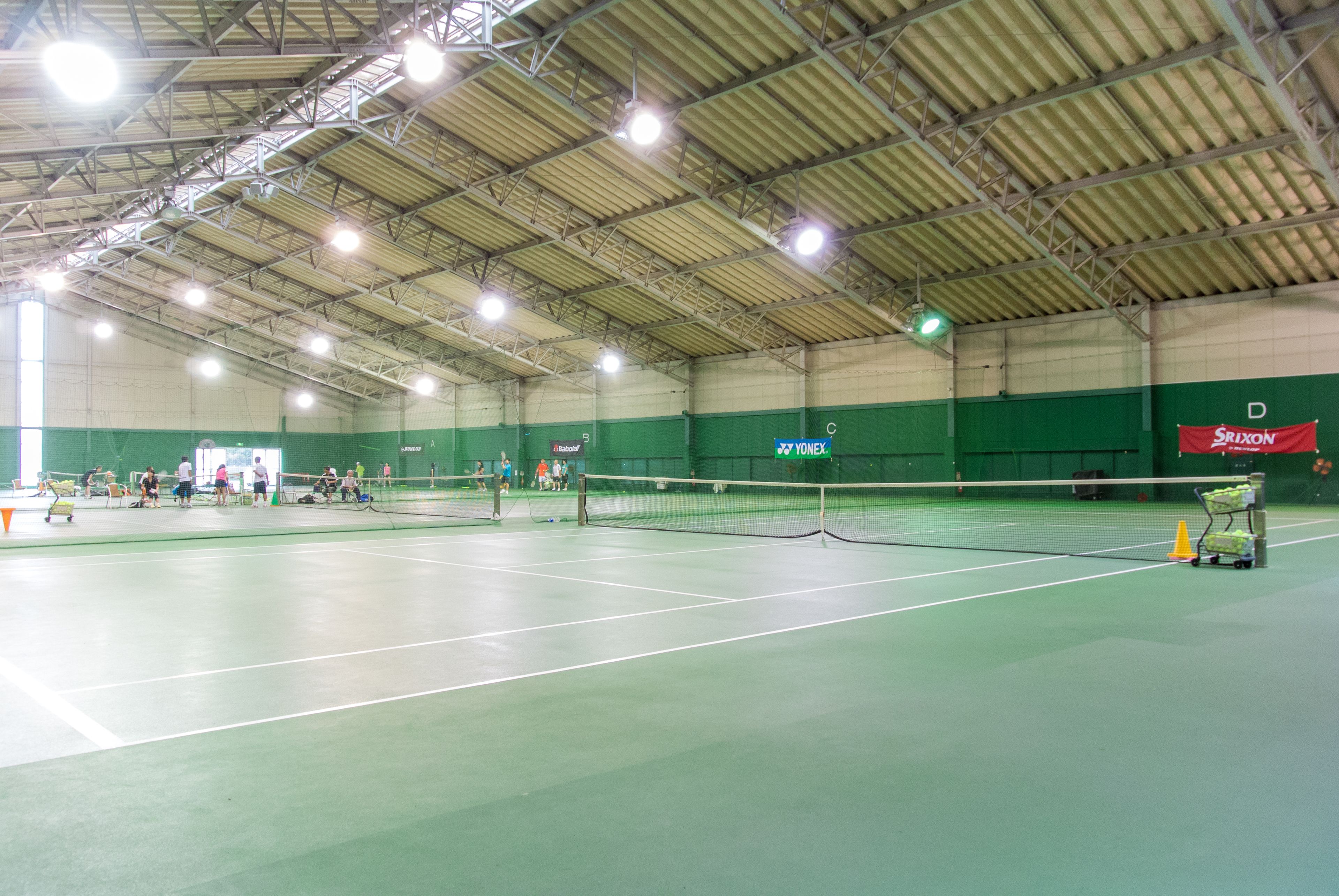 An indoor tennis court with multiple courts, a net, and a green wall with sponsor logos.