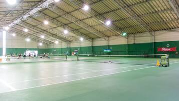 An indoor tennis court with multiple courts, a net, and a green wall with sponsor logos.
