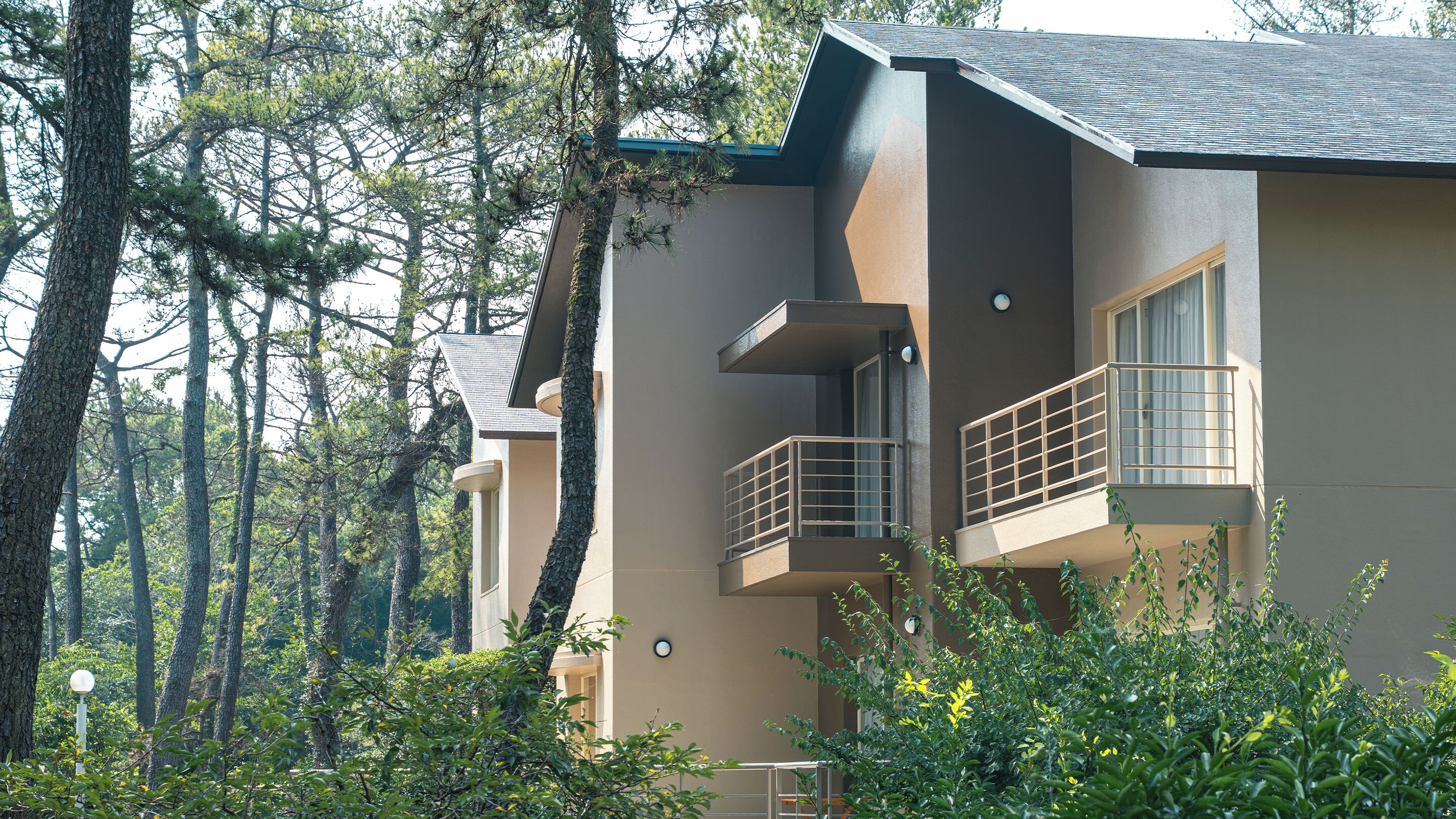 A modern two-story building with balconies, surrounded by dense forest.