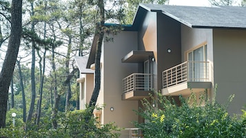 Un edificio moderno de dos pisos con balcones, rodeado de un bosque denso.