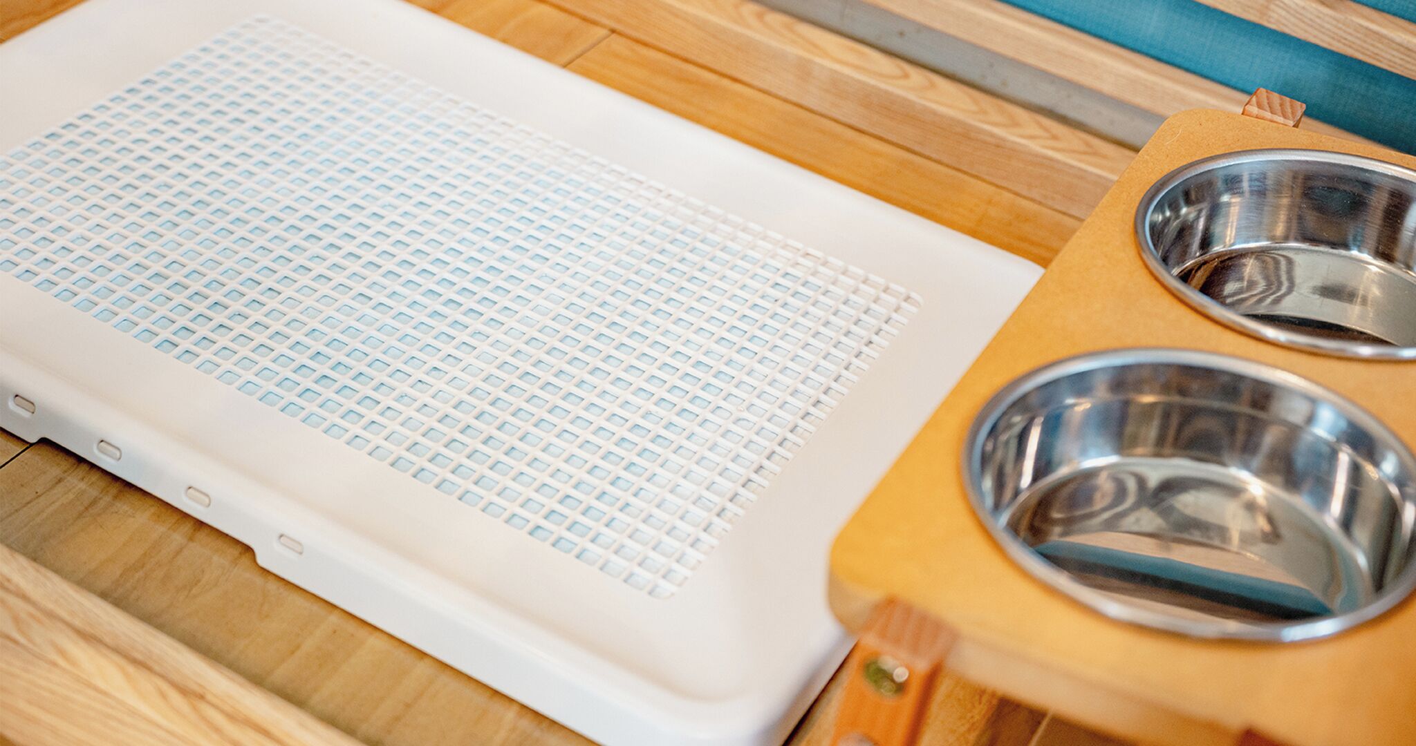 Un panier pour animal de compagnie avec une surface en forme de grille et deux gamelles en métal, posés sur une table en bois.
