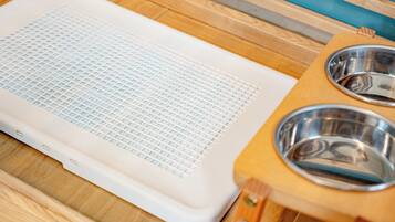 Un panier pour animal de compagnie avec une surface en forme de grille et deux gamelles en métal, posés sur une table en bois.