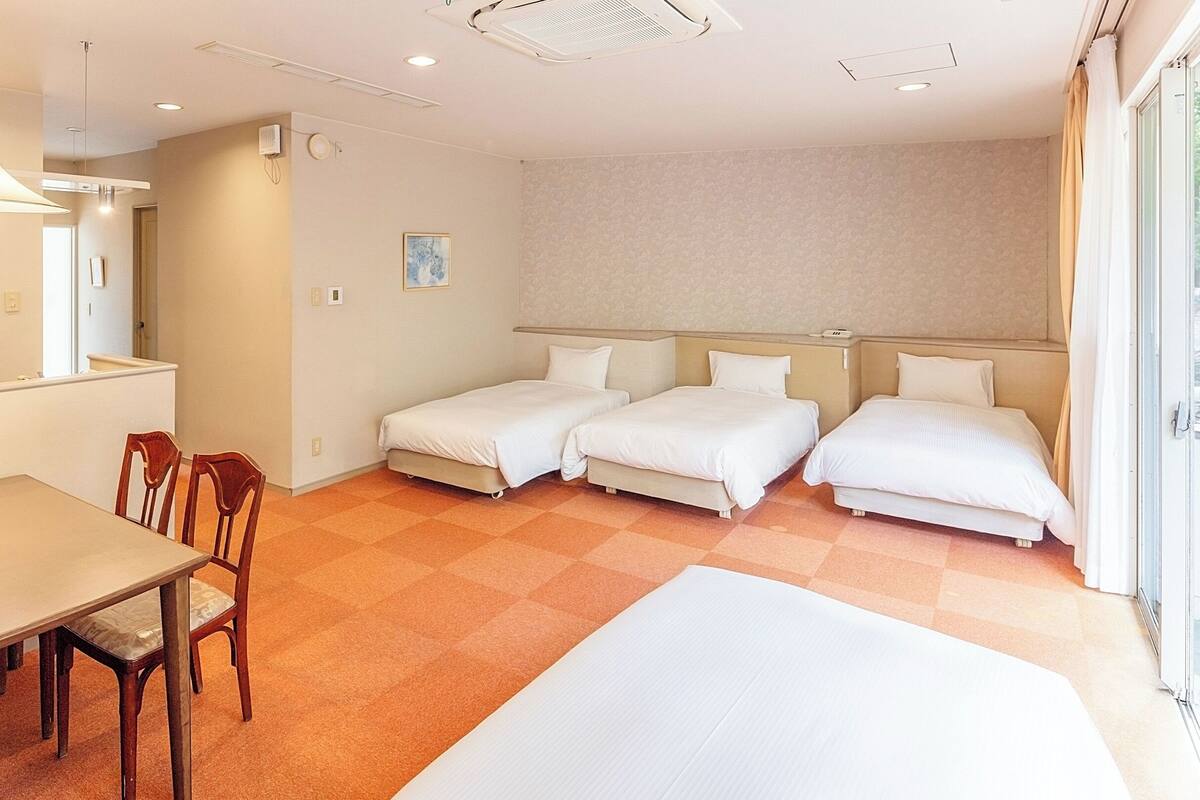 A hotel room with a dining table, two single beds, and a large bed.