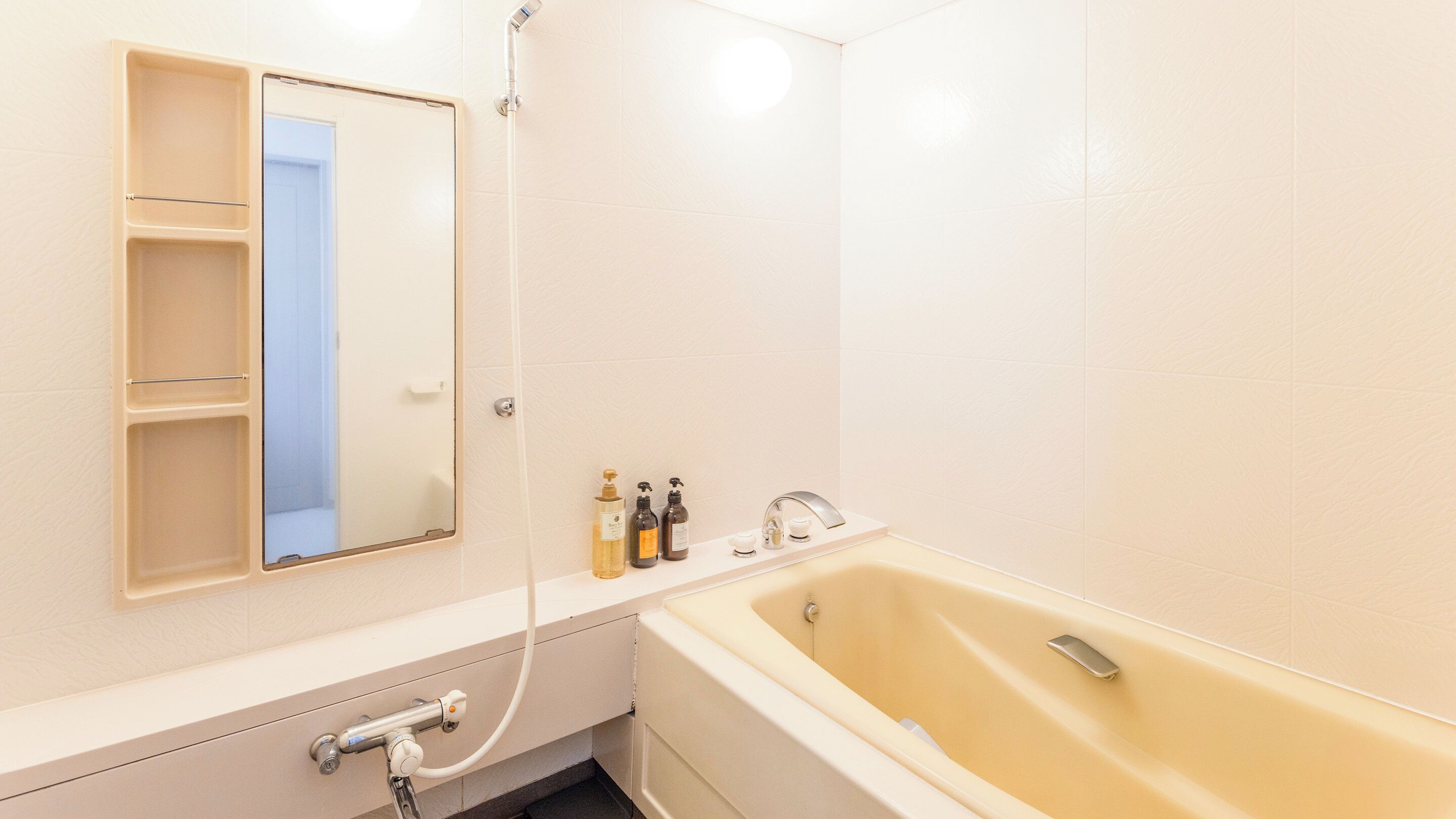 Un baño con bañera, espejo, repisas con artículos de aseo y ducha.