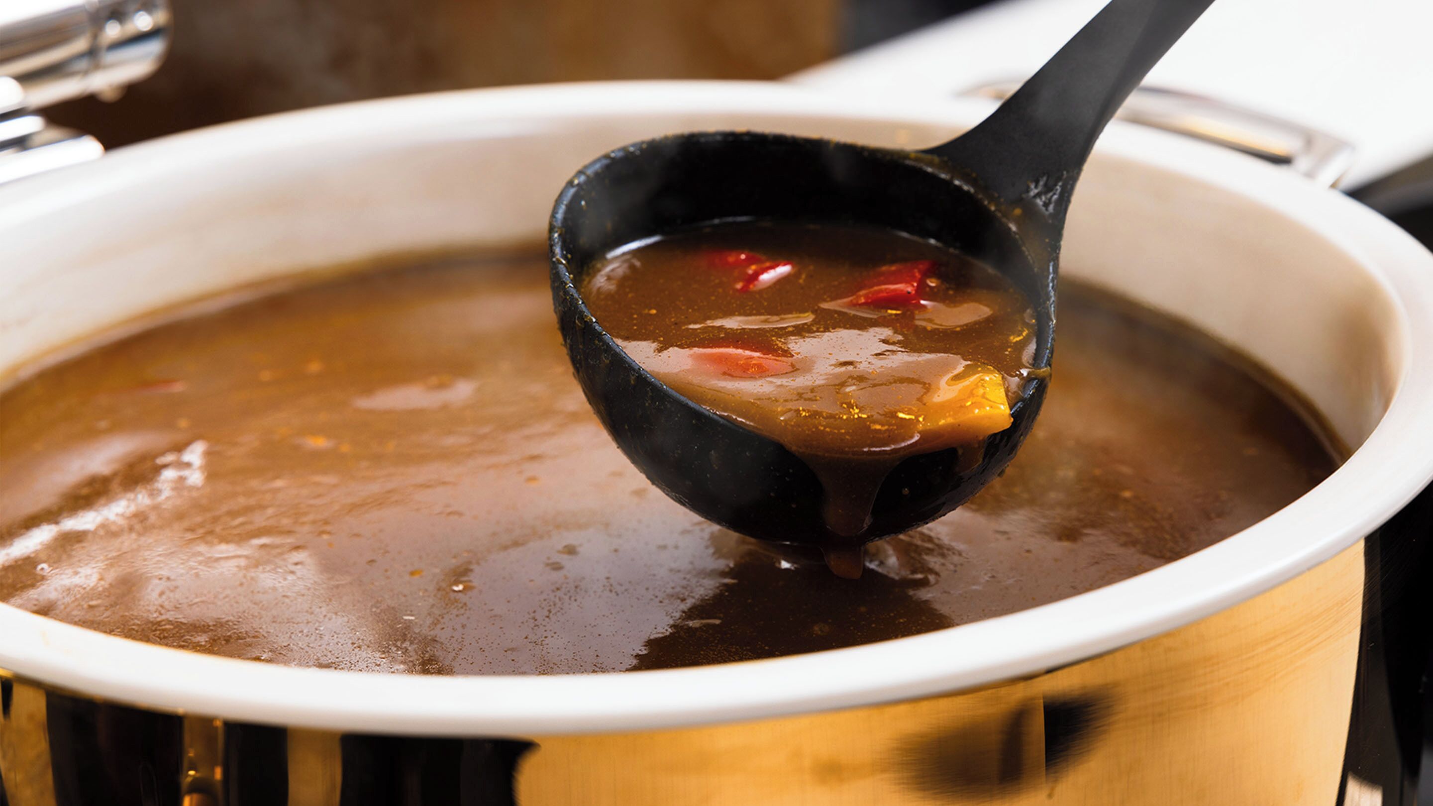 A ladle lifting soup from a pot.