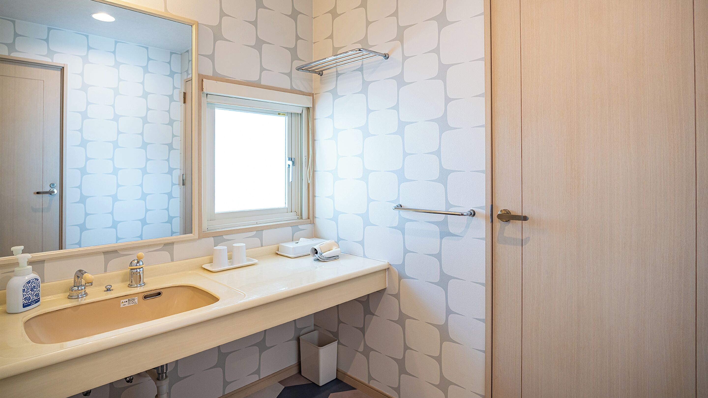 Un baño con lavamanos, espejo, toallero y una puerta.