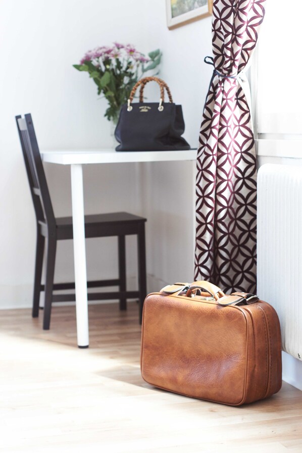 A brown suitcase on a wooden floor next to a white table with a dark handbag on it. - Pensionat Augustin (Gällivare)