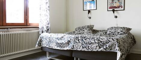 A bedroom with a bed, a radiator, and two framed pictures on the wall.