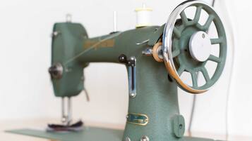 Une machine à coudre ancienne, de couleur verte, dotée d’une roue en métal et d’une bobine de fil.