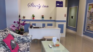 A reception area with a reception desk, a couch with a decorative pillow, and a sign that reads "Slowly inn". - Slowly Inn (Hengchun)