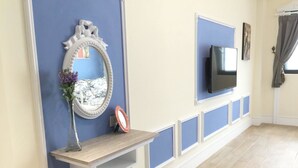 A room with a blue accent wall, a mounted TV, a small table with a vase and a picture frame, and a bench. - Slowly Inn (Hengchun)