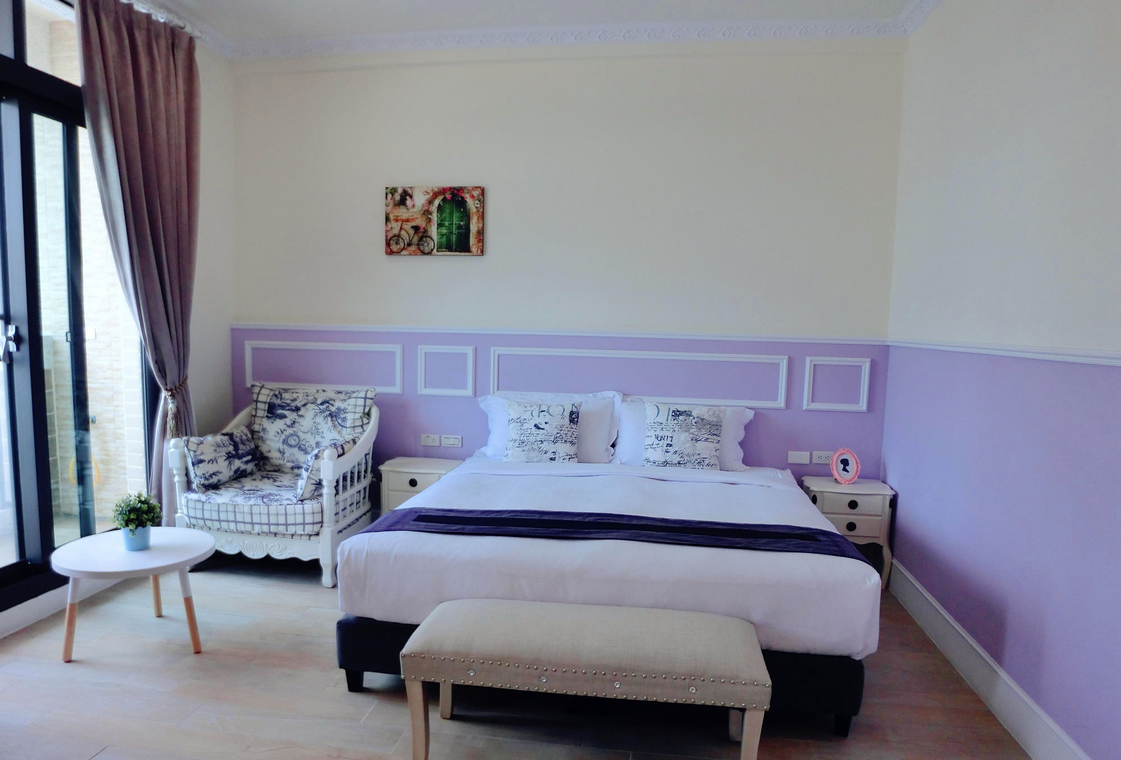 Un dormitorio con cama, una silla, una mesita y un banco.