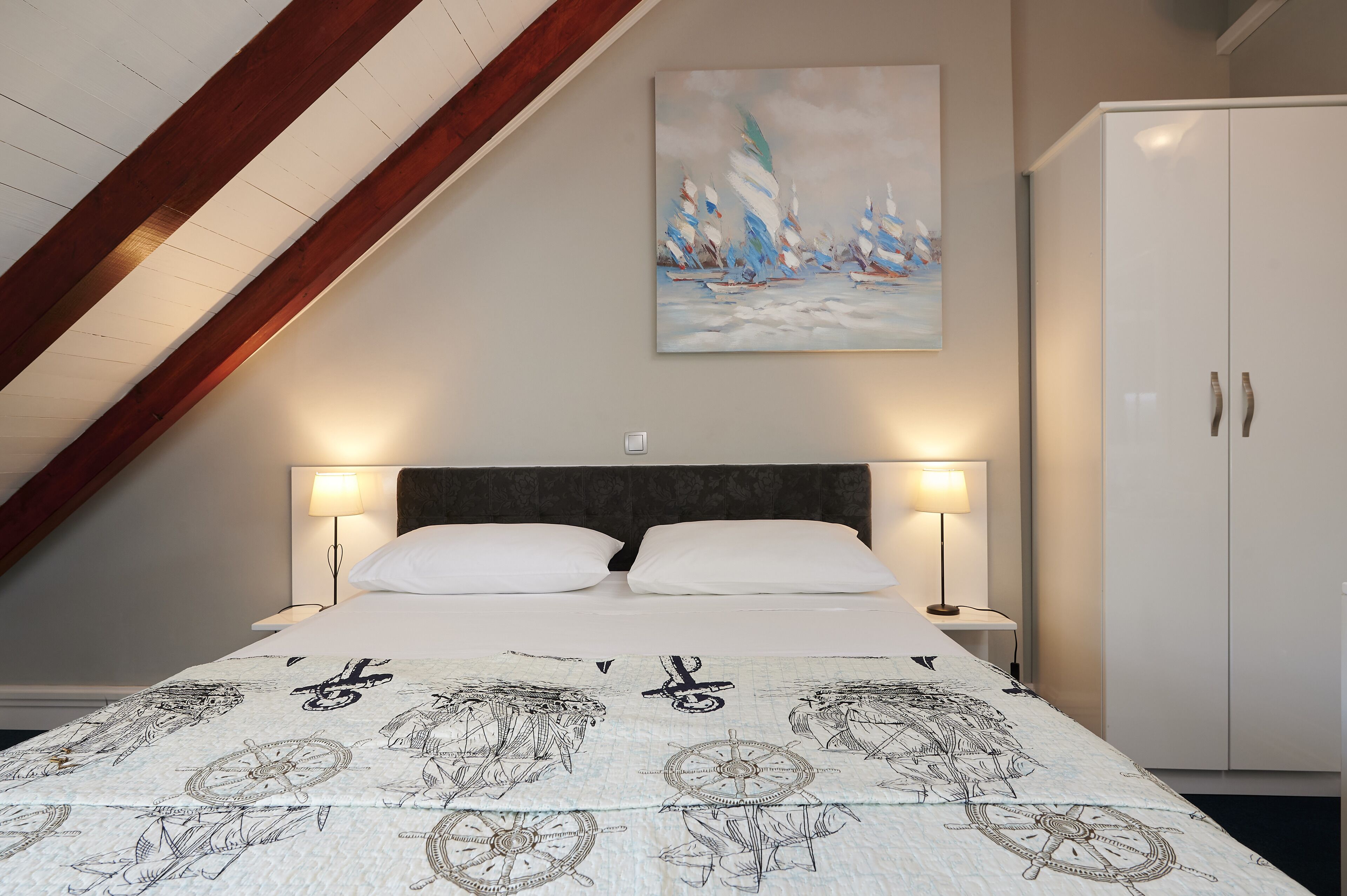 A bedroom with a bed, two bedside lamps, a headboard, a painting on the wall, and a wardrobe.