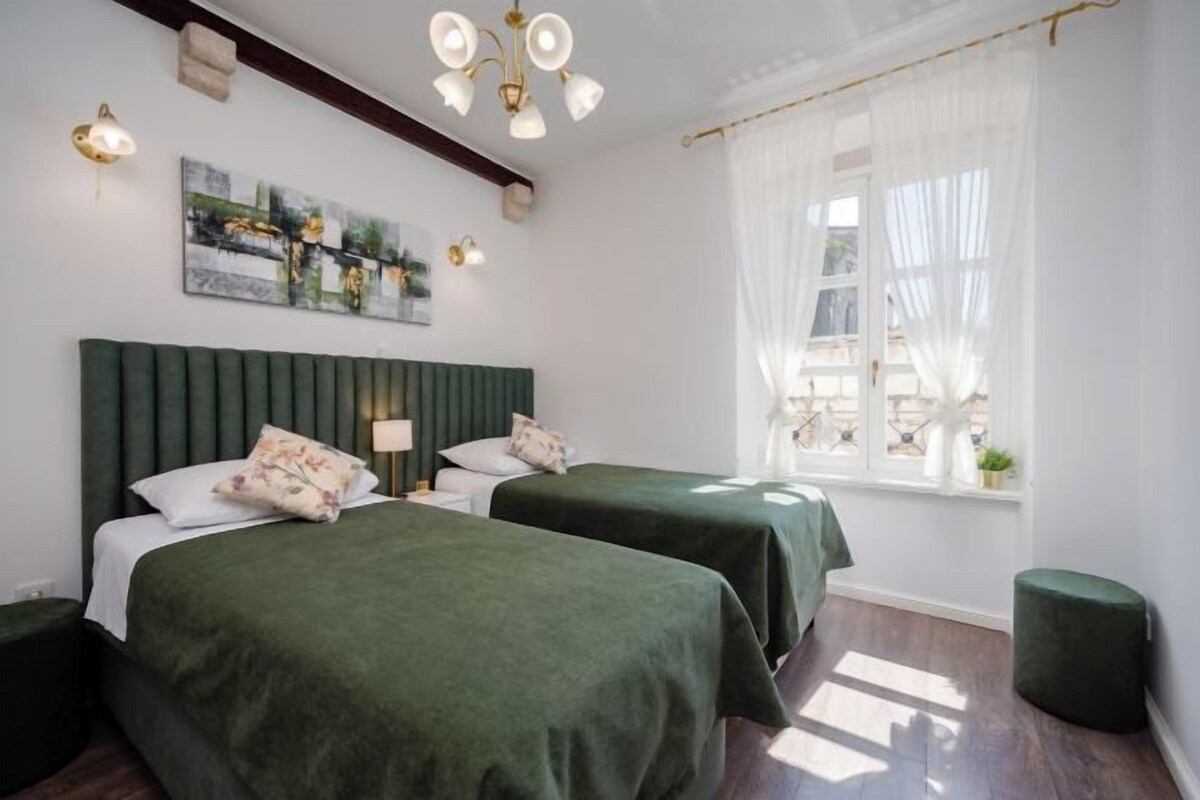 Una habitación con dos camas, una ventana con cortinas, un cuadro en la pared y un candelabro.