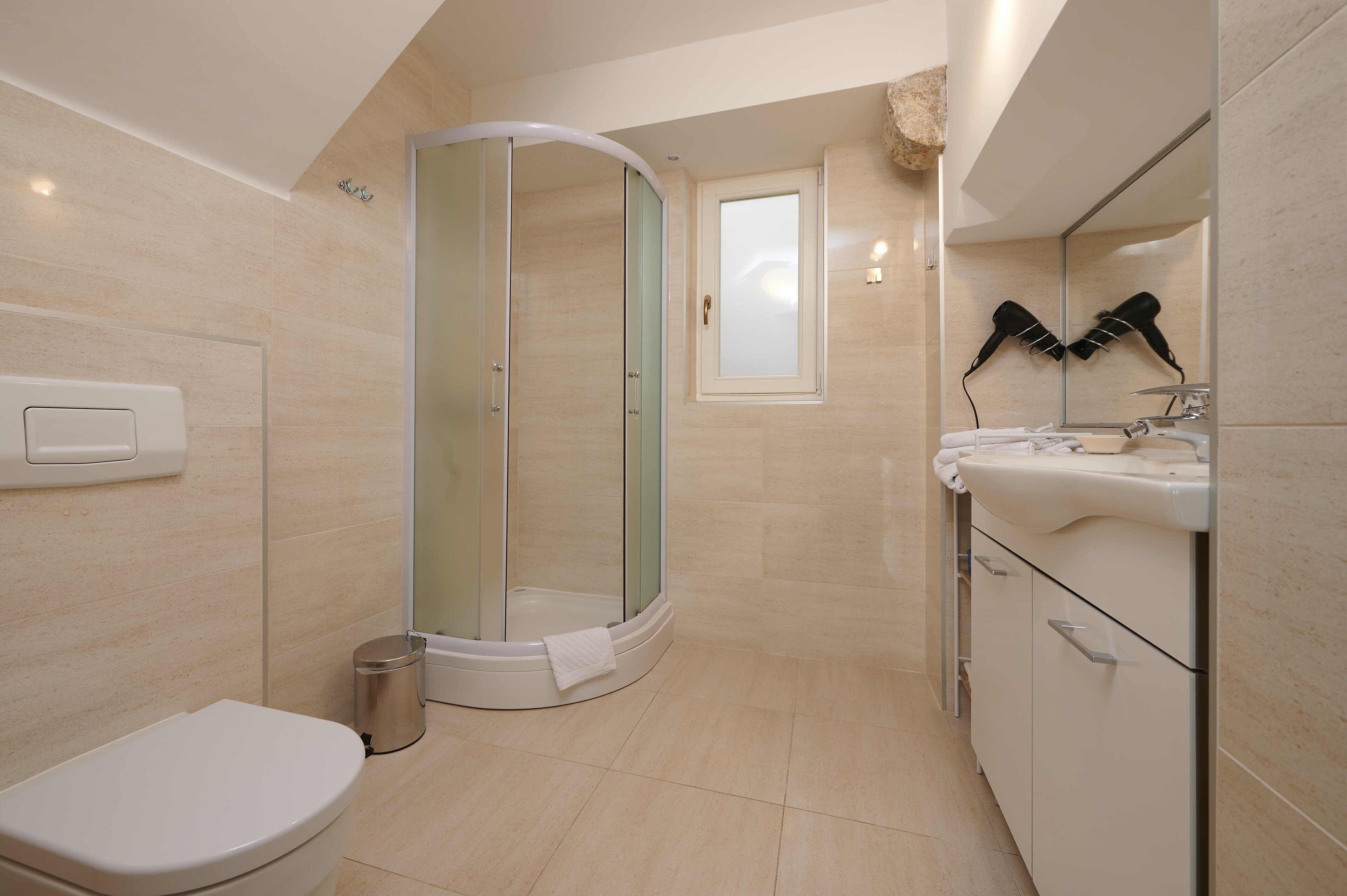 A modern bathroom with a glass-enclosed shower, a toilet, a sink with a mirror, and a hairdryer mounted on the wall.