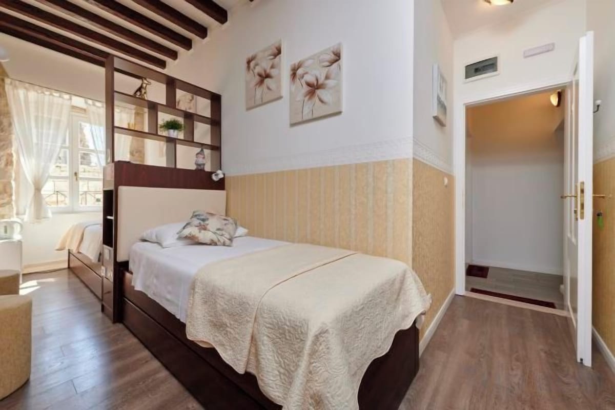 A bedroom with a single bed, a wardrobe, a bedside table, and a window with curtains.