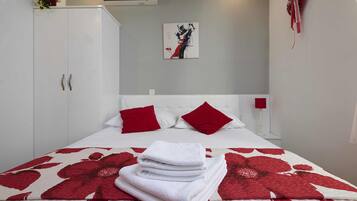 Una cama bien hecha con una colcha floral roja y blanca, una pila de toallas blancas y dos almohadas rojas.
