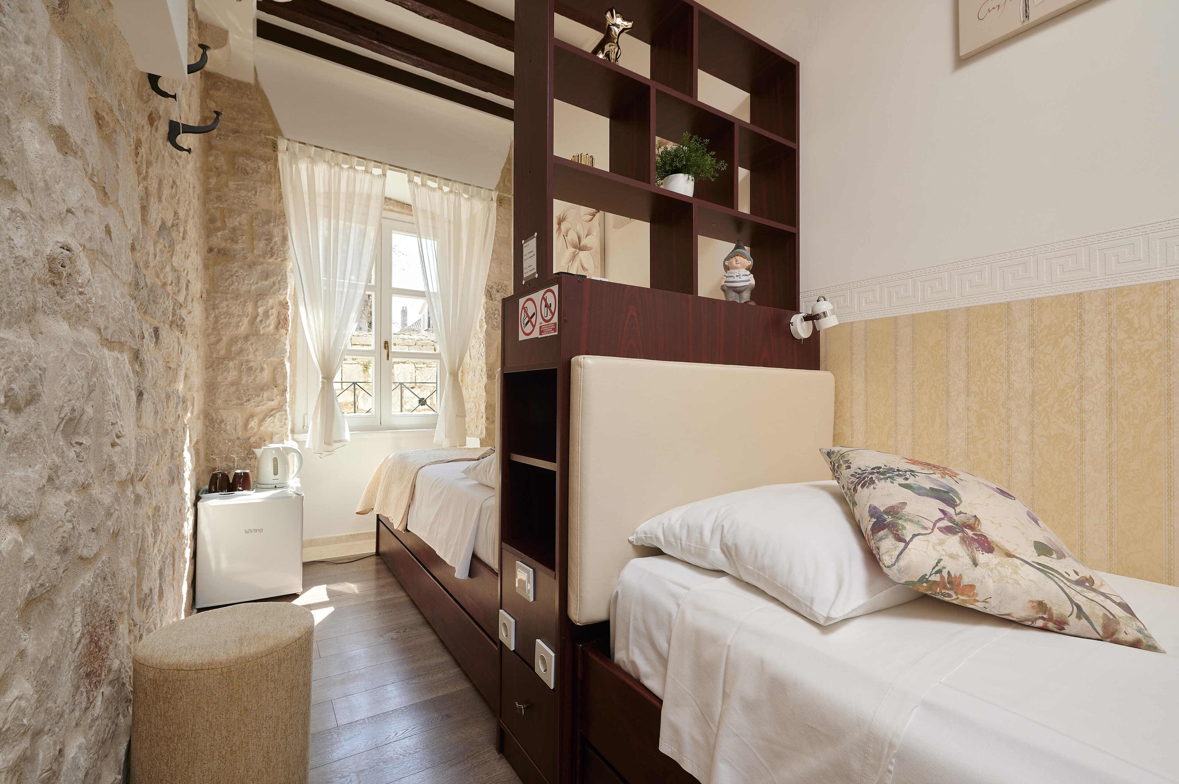 A bedroom with a bunk bed, a bedside table, a small white cabinet, and a window with curtains.