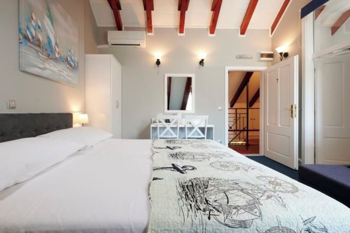 A bedroom with a bed, a desk, a chair, and a mirror. There is a staircase leading to another room.